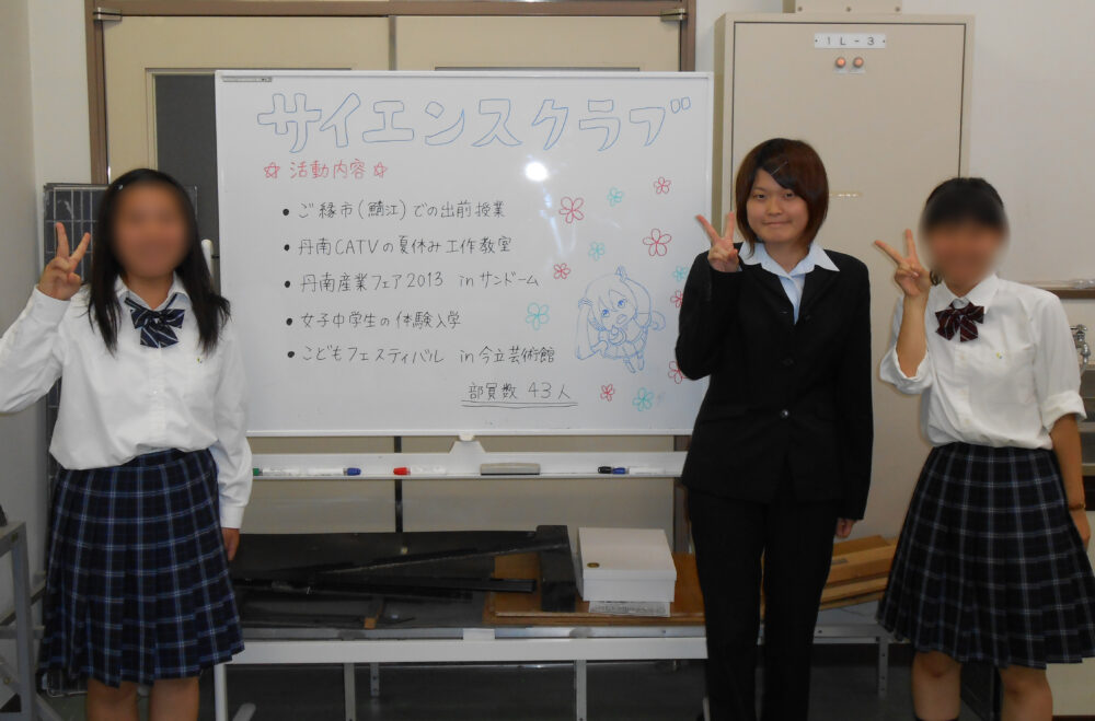 制服姿の女子学生2名と、ホワイトボードを囲んでピースサイン